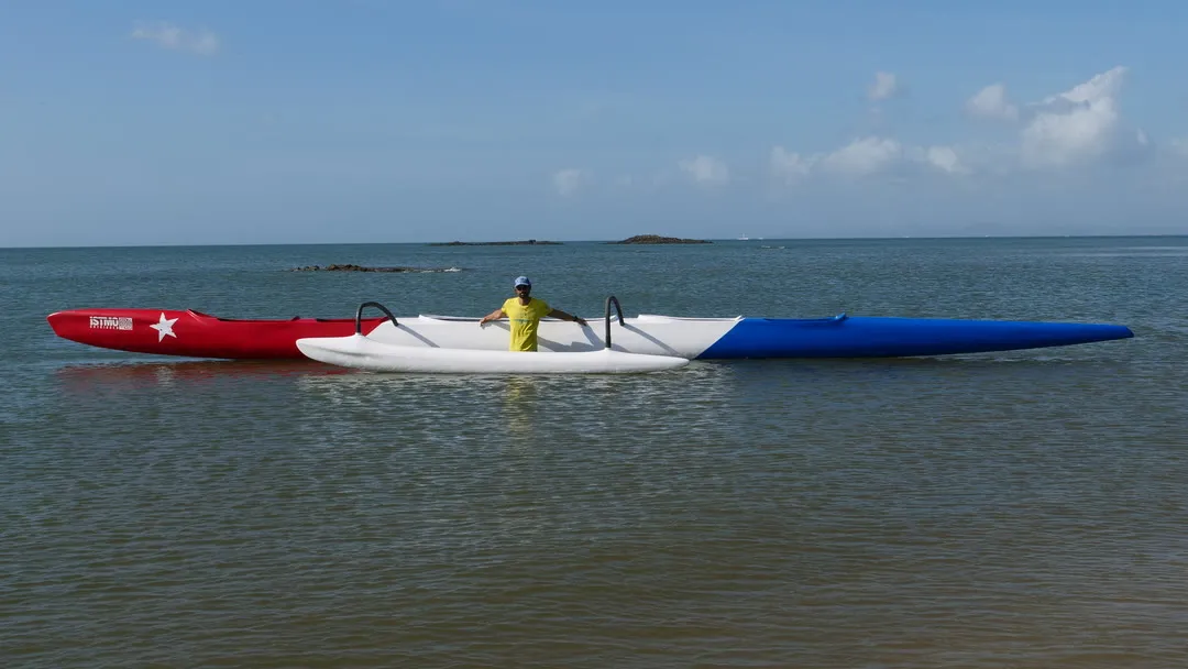 Canoa OC-6 completa en aguas someras; una persona de pie junto al casco da la escala.