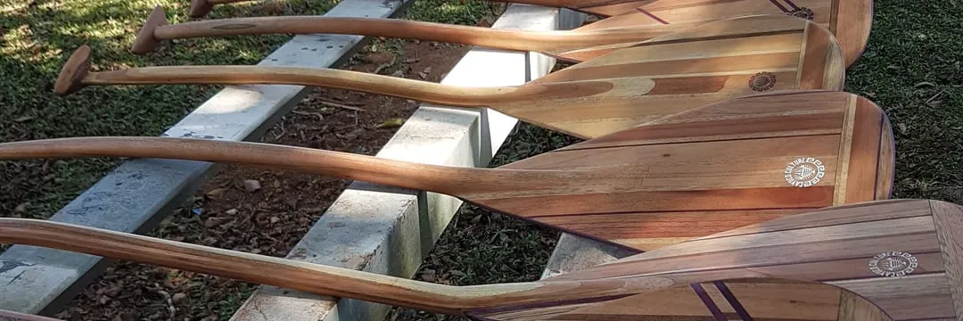 Remos de cayuco en madera laminada, con listones de contraste y el sello Cayuco Culture en el remo.
